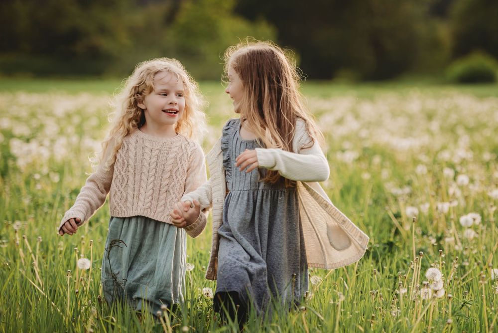 Two people sitting together in a meadow filled with white dandelions on a sunny spring day.