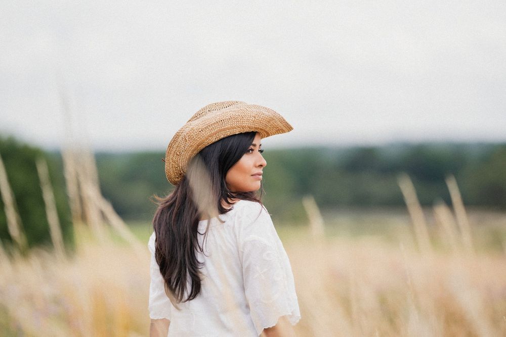 Someone wearing a wide-brimmed sun hat stands in a grassy meadow against a scenic mountain backdrop.