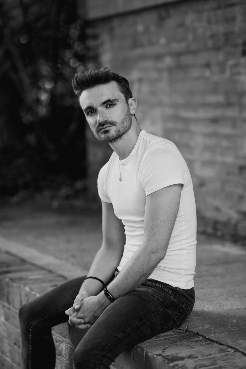 Moody black and white portrait series of someone sitting on steps wearing a white t-shirt and dark jeans.