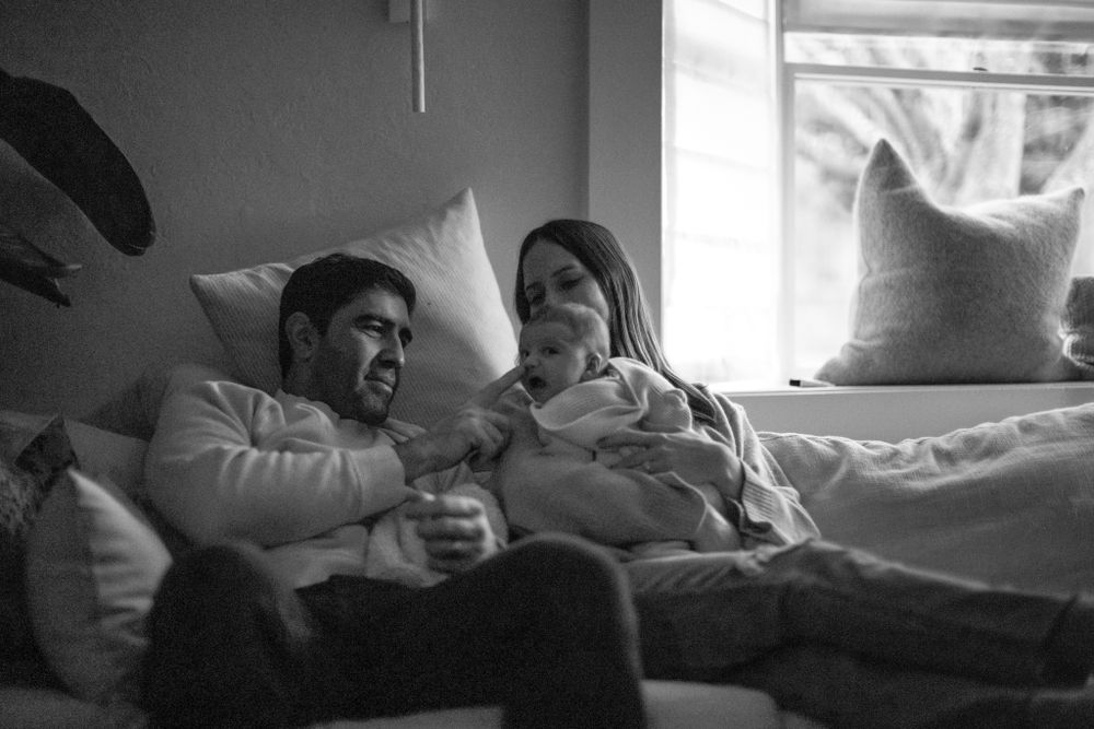 A cozy black and white image of a family relaxing together on a bed.