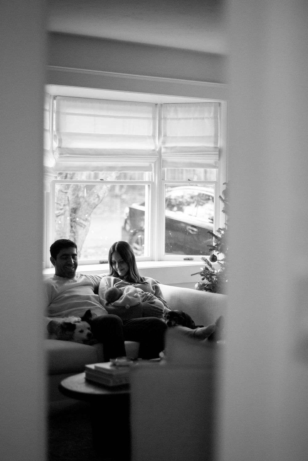 A black and white photo peeking through doorway at family relaxing by window.