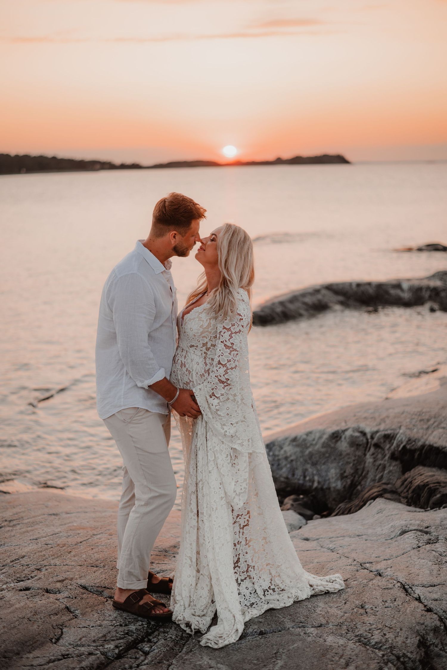 Gravidpar i solnedgången på klippor på torö