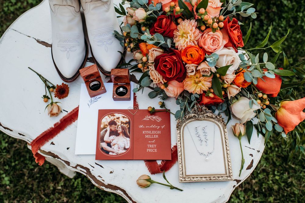 Elegant wedding stationery with coral roses and greenery arranged on grass featuring invitations and decorative elements.