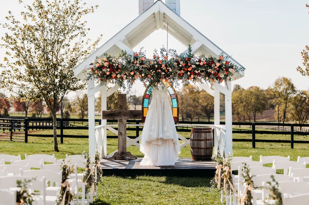 A white wedding gazebo decorated with autumn floral arrangements and white chairs set up for an outdoor ceremony.