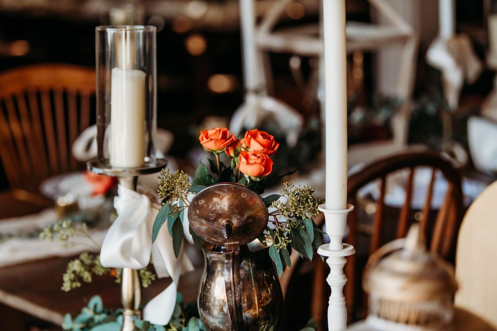 Elegant wedding reception table decorated with white candles, copper accents, and delicate floral arrangements.