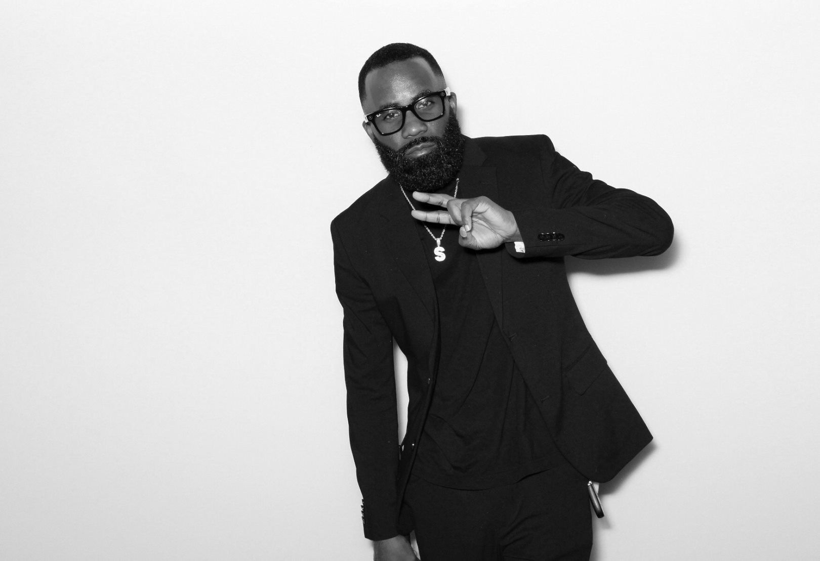 Photographer with a well-groomed beard holds a camera lens while wearing a dark sweatshirt against brown backdrop.