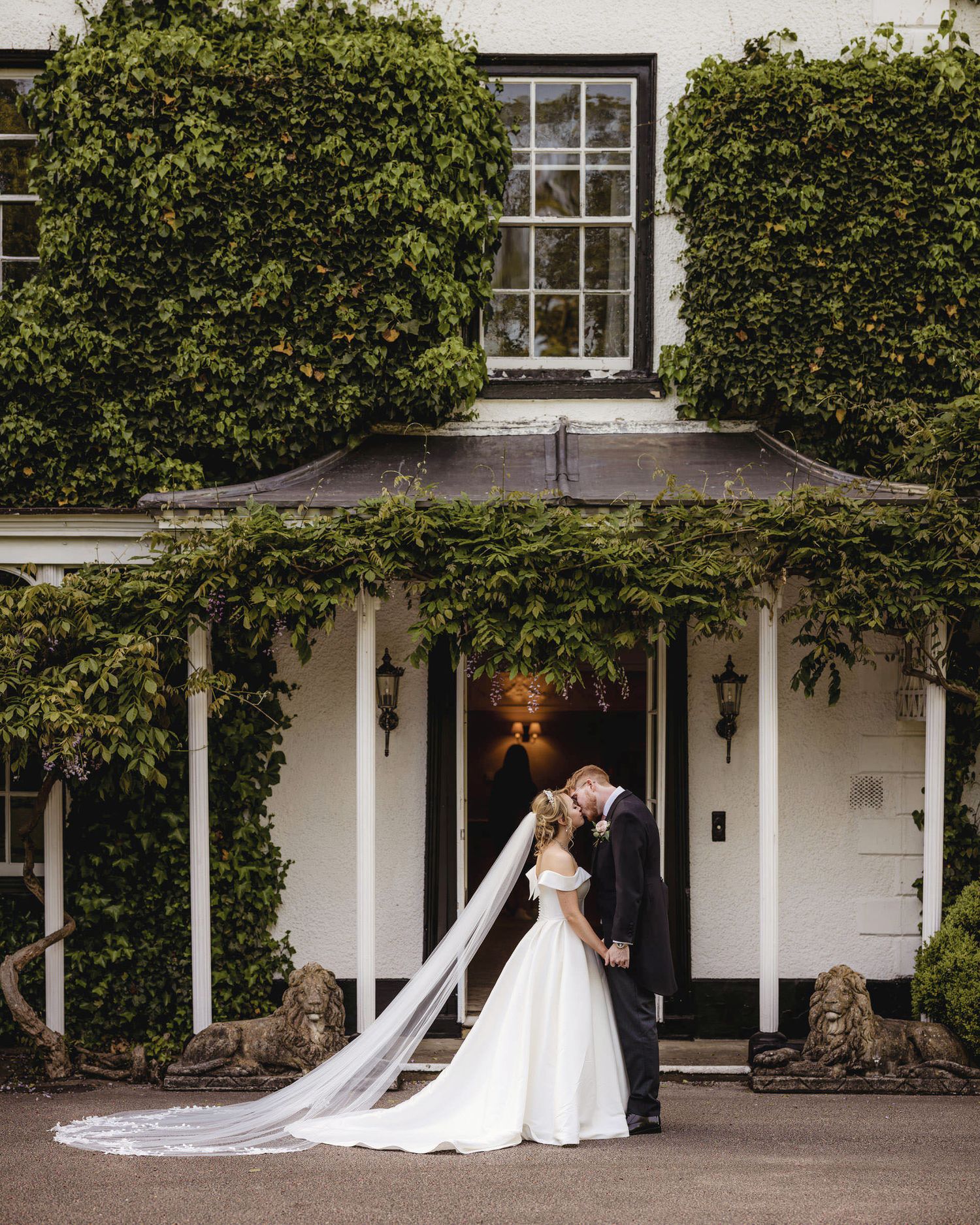 Bride in white wedding dress stands with her smartly suited groom in a forest of tall trees at Peckforton Castle