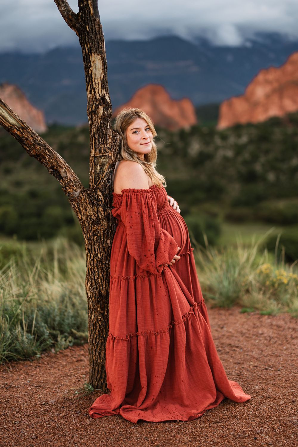 Person in flowing red dress poses against dramatic backdrop of Garden of the Gods park in Colorado Springs at sunset.