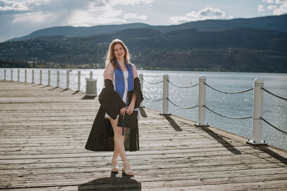 A scenic wooden pier stretches out across a mountain lake on a cloudy day with roped railings along the edges. A university grad is proud.