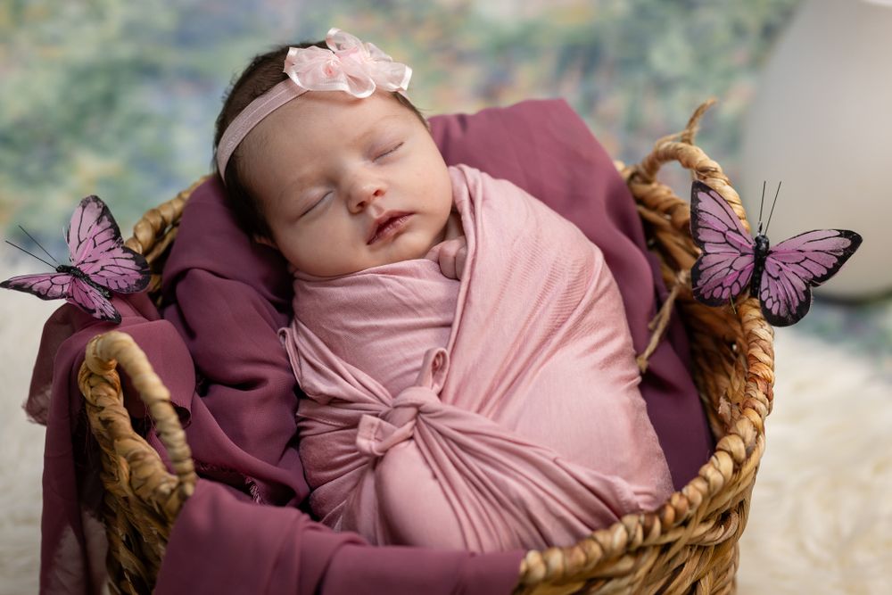 Newborn in a pink wrap and bow headband nestled in a basket during a studio session in Mountain Home, Arkansas
