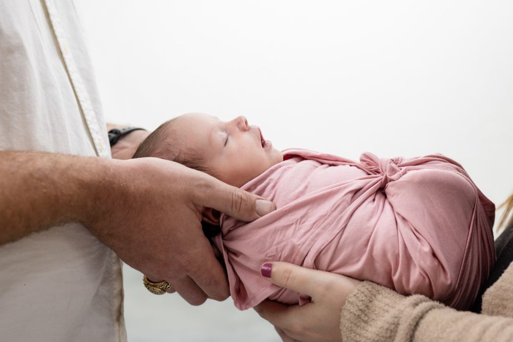 Newborn in a pink wrap cradled in hands during a studio session in Mountain Home, Arkansas