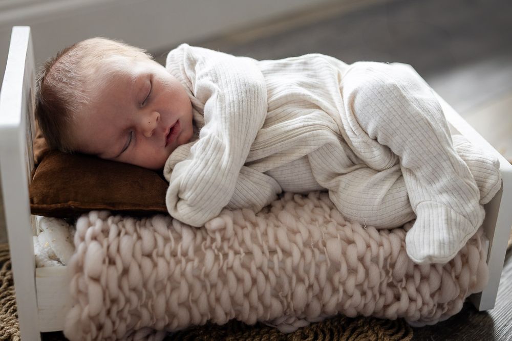 Sleeping newborn in a white outfit on a knit blanket during a studio session in Mountain Home, Arkansas