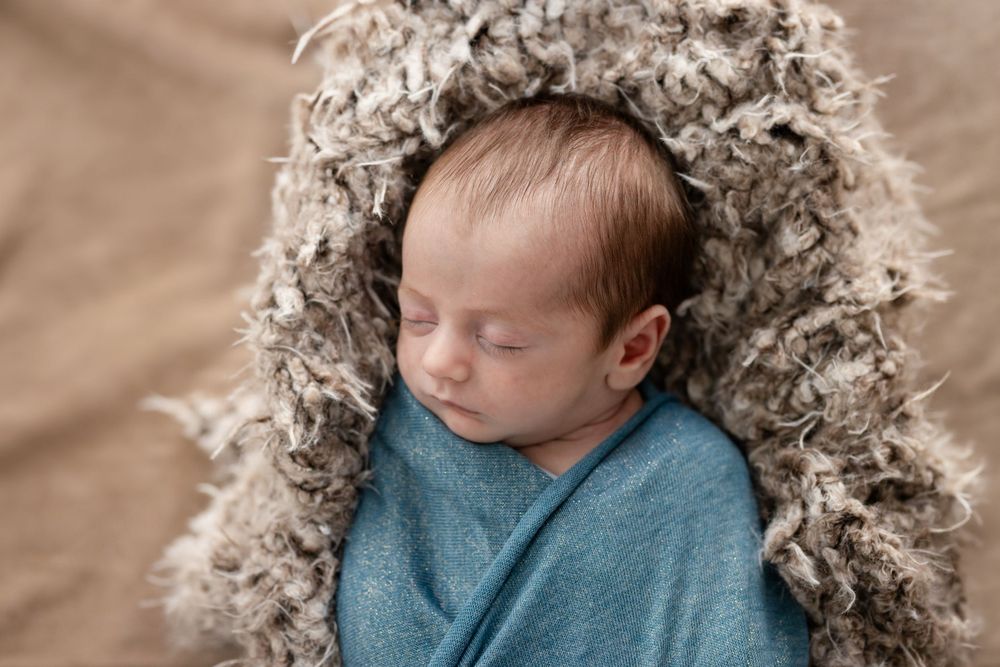 Sleeping newborn in a teal wrap on a fur layer during a studio session in Mountain Home, Arkansas