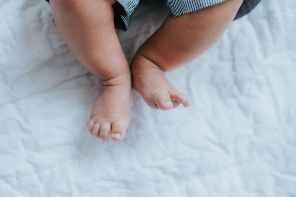 Close-up view of tiny baby feet resting on white textured bedding.