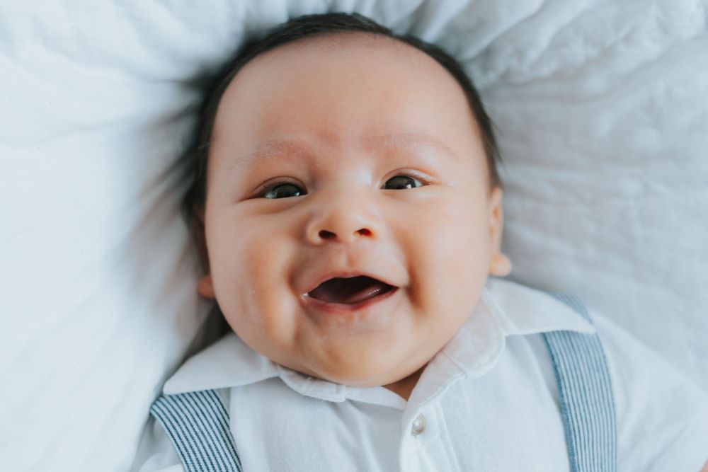 Infant lying on white bedding wearing a light blue outfit.