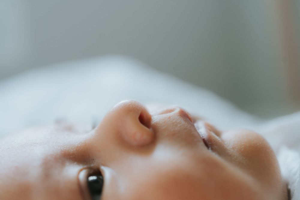 An extreme close-up view of a baby's face showing one eye and nose against a soft, light background.