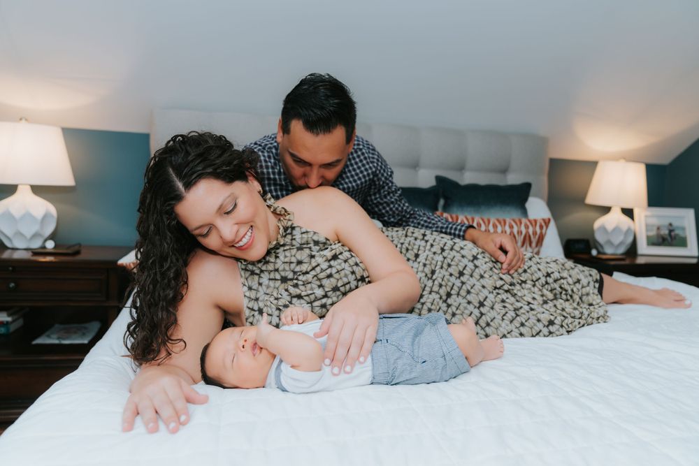 A family cuddles together on a white bed in a cozy bedroom with matching table lamps.