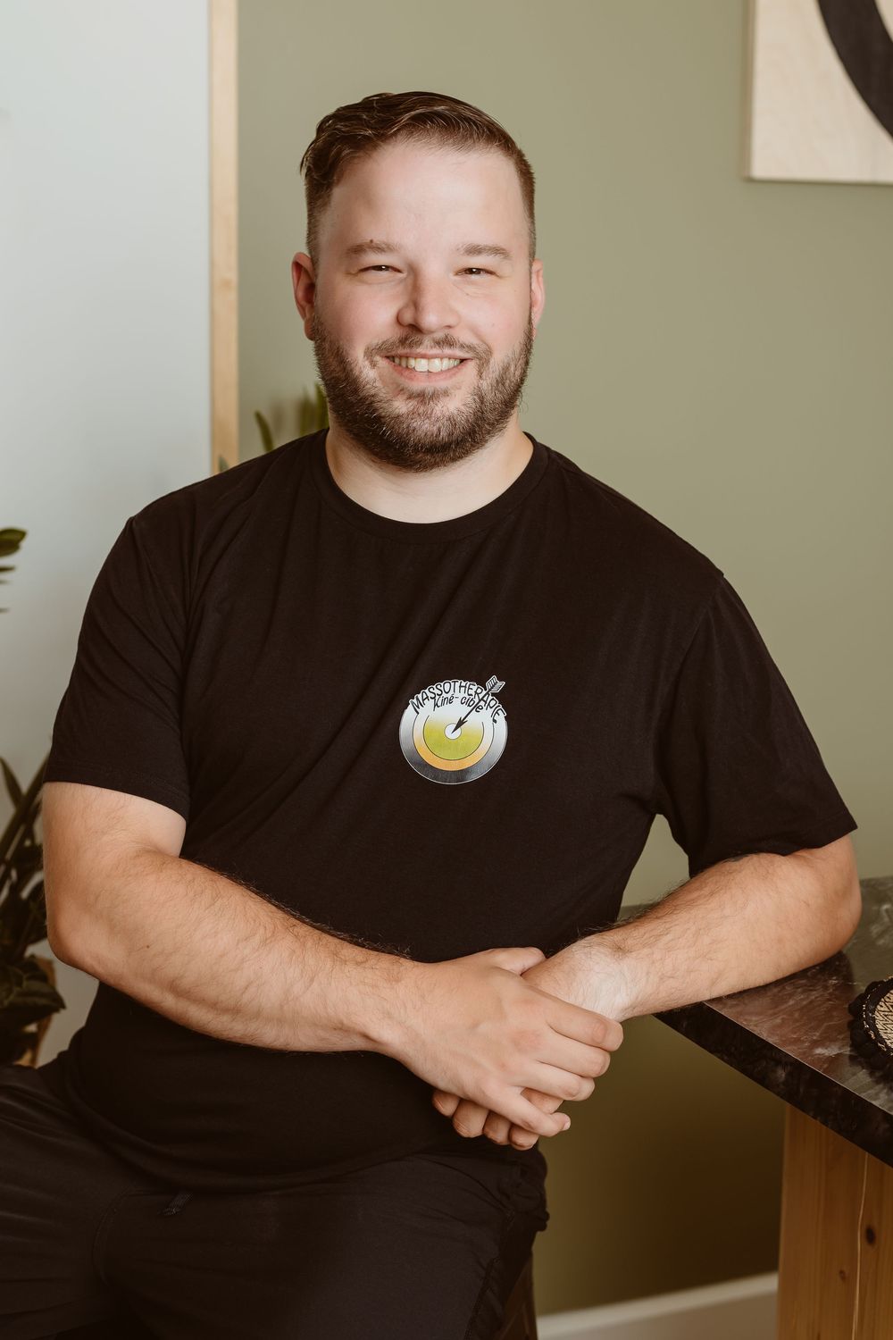 A man wearing a black t-shirt with a logo smiles while posing for professional headshots in a studio setting.