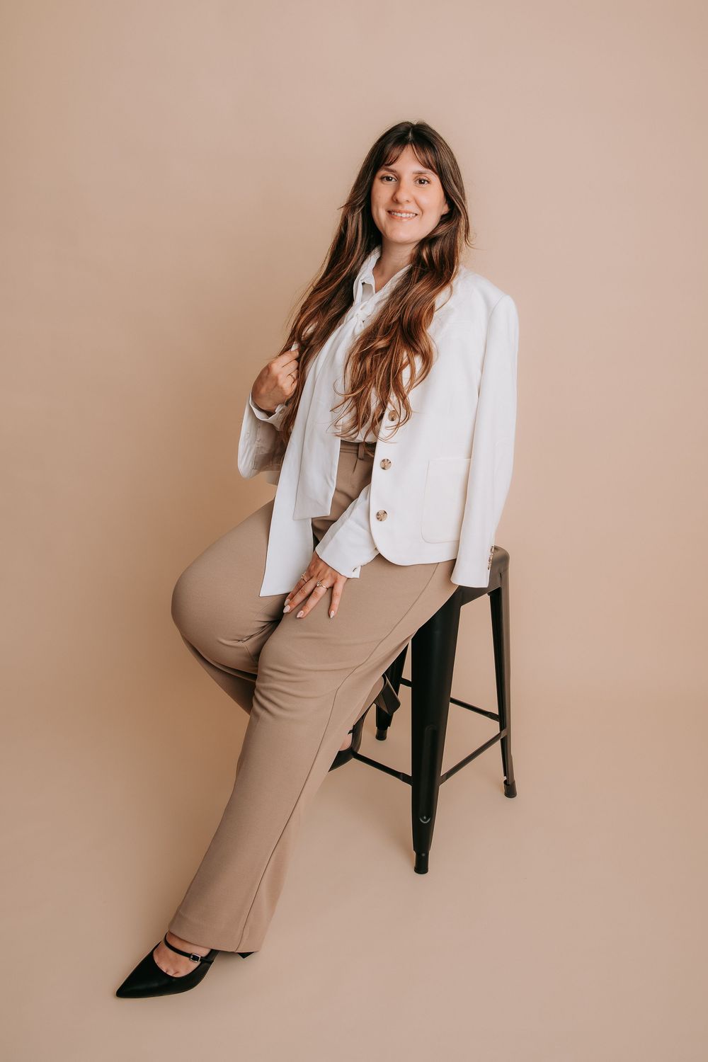 Professional studio portraits of a woman in a white blazer and beige skirt posing on a stool against neutral backdrop.
