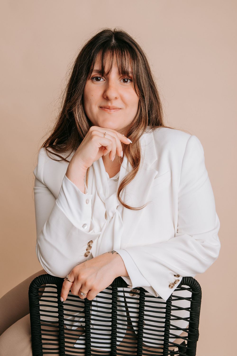 Person in white button-down shirt poses on striped chair against beige background in artistic photo series.