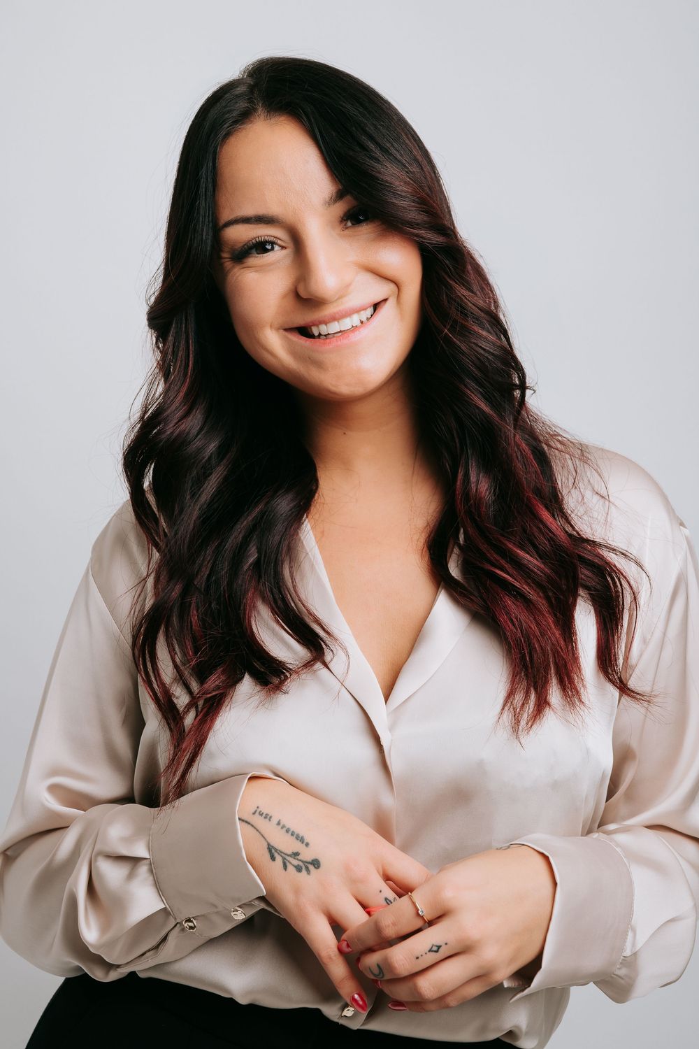 Professional portrait of someone wearing a cream silk blouse with long dark hair smiling warmly against a light background.