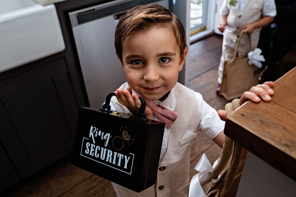 A child in a white shirt holds up a black lunchbox with the word 'Security' written on it at a dining table.