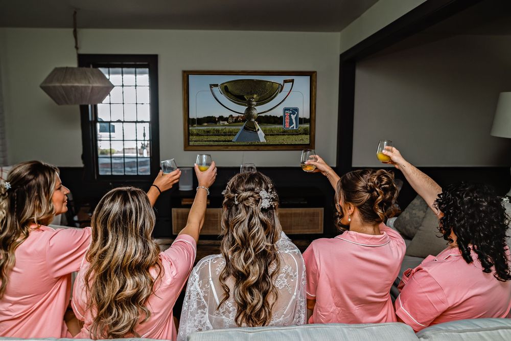 Wedding party in matching pink robes raises their hands in celebration while posing for a group photo.