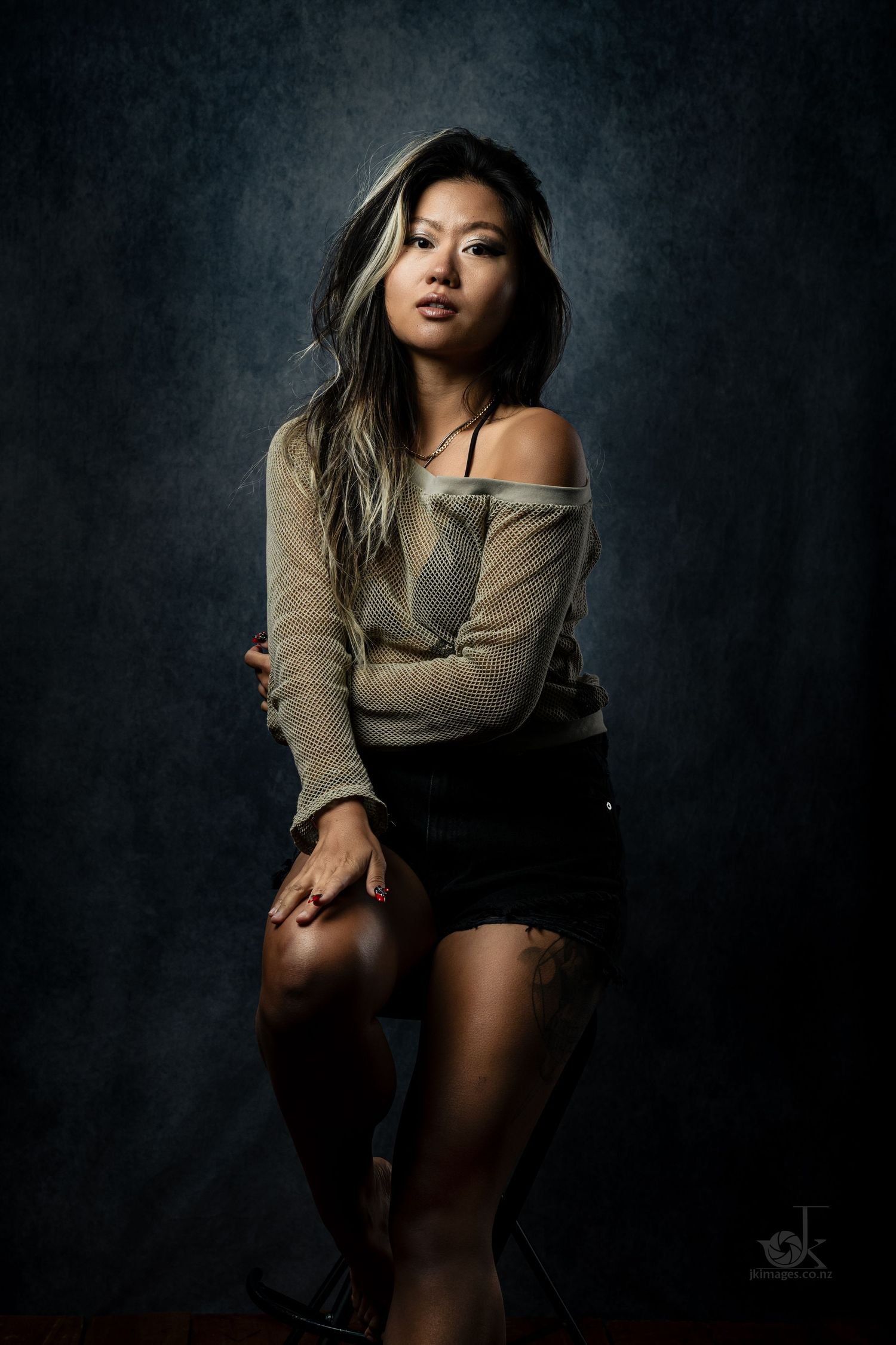 Dramatic portrait against dark background with off-shoulder sweater and shorts in moody lighting.