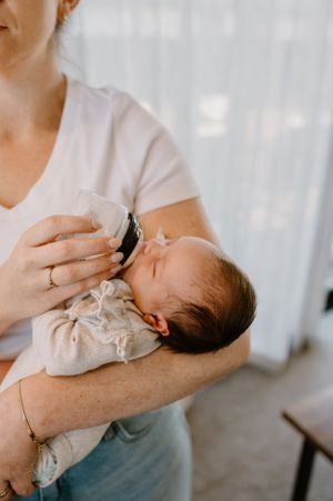 A peaceful moment as a tiny newborn is bottle fed in front of sheer white curtains.