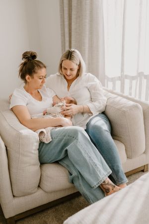 A relaxed moment on a grey couch as a newborn receives care and attention.