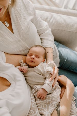 A peaceful newborn in a ruffled onesie sleeps contentedly on a couch.
