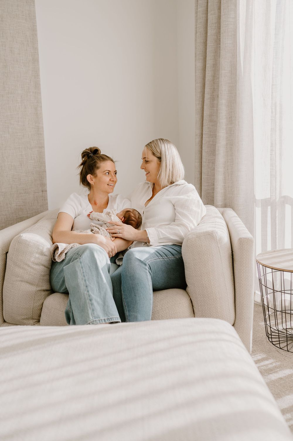 A joyful moment shared on a grey couch while caring for a newborn.