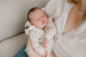 A sleeping newborn in white clothing rests peacefully on soft fabric.