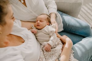 A sleeping newborn baby rests peacefully on a couch with caretakers nearby.
