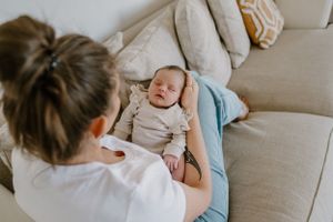 A sleeping infant in light colored clothing rests peacefully on a grey couch.