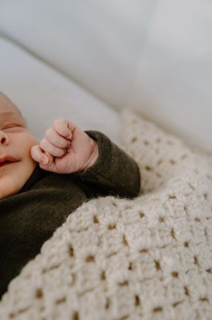 Close-up of a tiny infant's hand against a white knitted blanket.