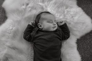 Black and white portrait of sleeping baby on fluffy white fur rug.