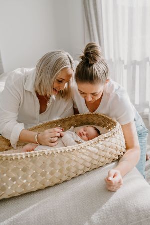 A peaceful moment as two people look at a baby resting in a woven bassinet.