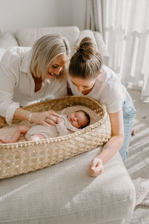A tender moment as caregivers watch over a sleeping infant in a woven basket.