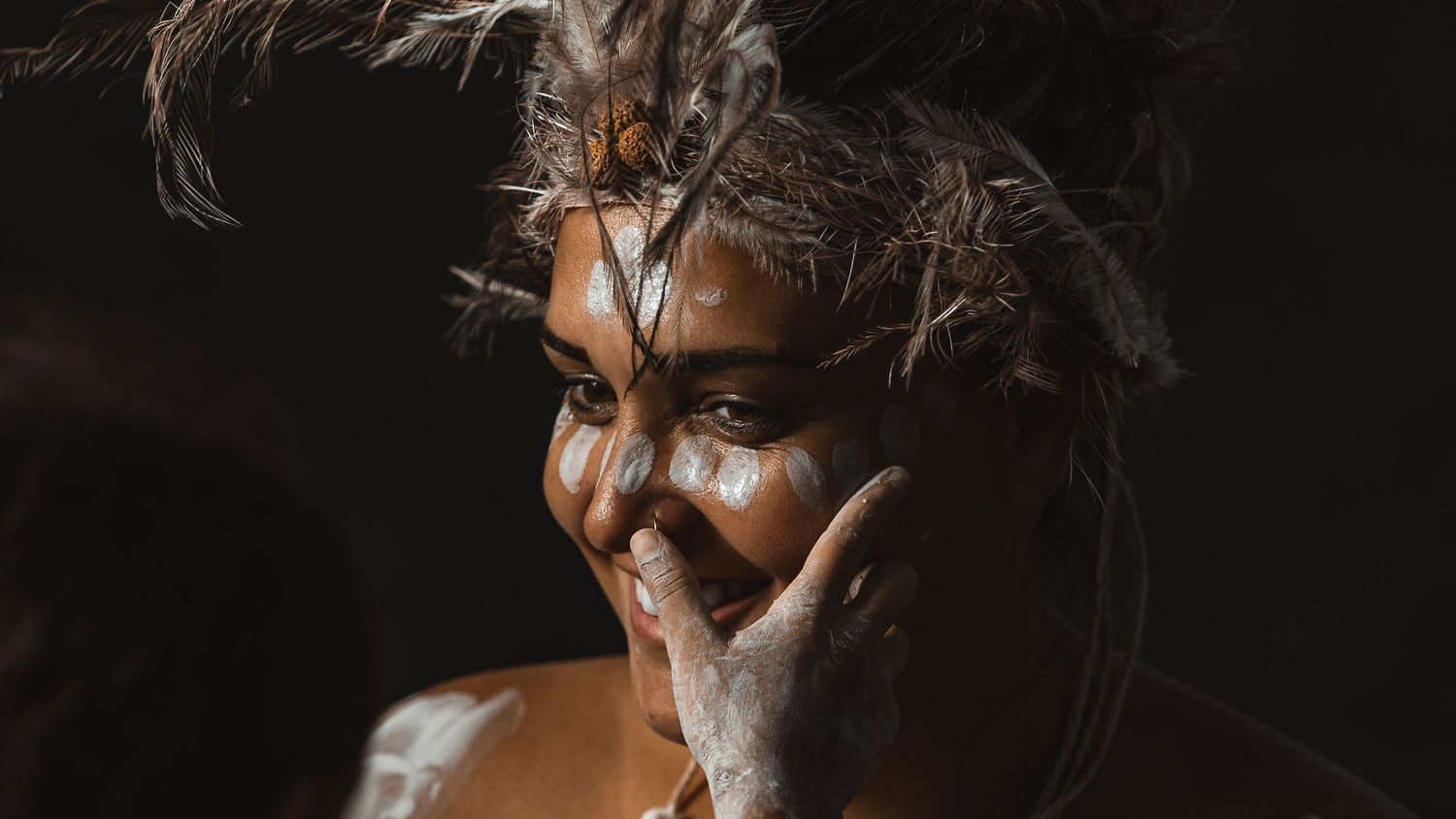 Dramatic close-up portrait with tribal face paint against dark background.