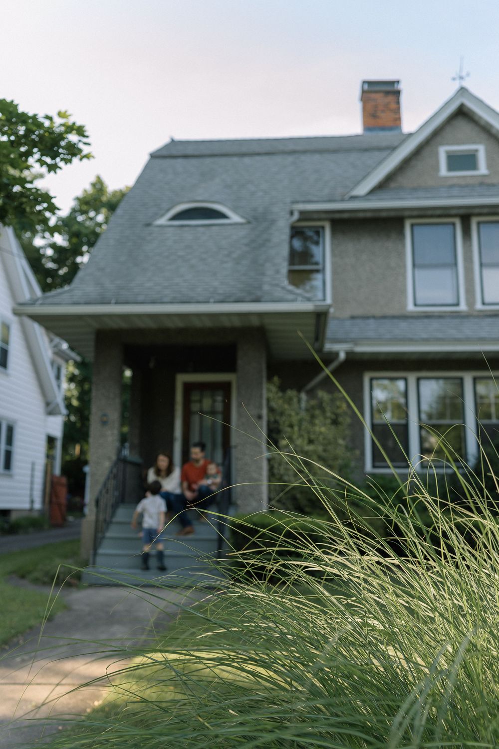 Grassy foreground frames a sequence of suburban houses with people standing on their porches at dusk.