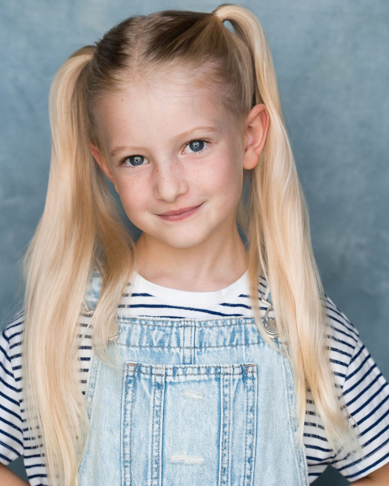 Studio portrait of young person in denim overalls and striped shirt with blonde pigtails. Actors headshots in Guildford, Surrey.