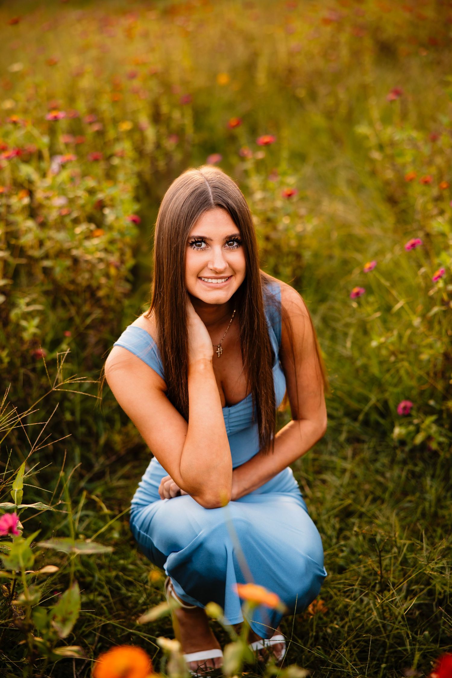 A person in a blue dress sits among vibrant wildflowers during a sunny outdoor portrait session.
