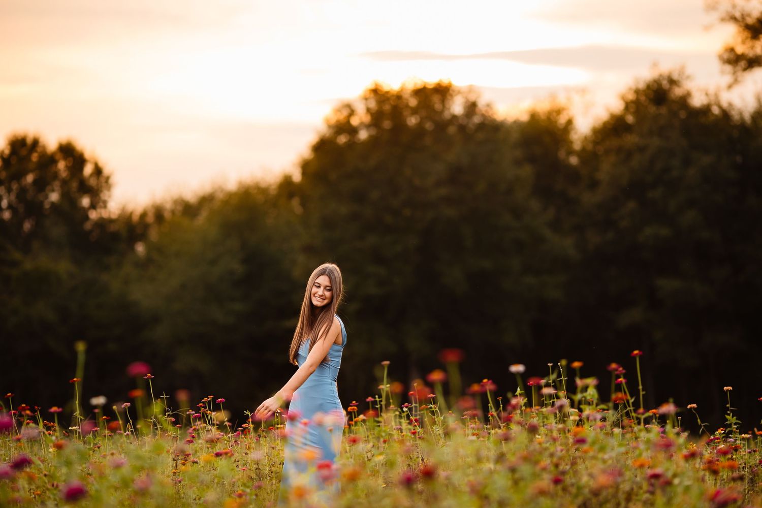 A person stands in a vibrant wildflower field during golden hour sunset with warm lighting and colorful blooms.
