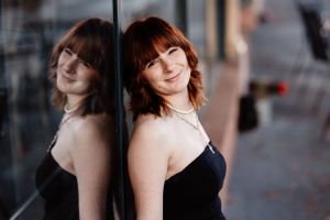 Girl Senior Portrait of woman in black dress with reflection in window during evening light.