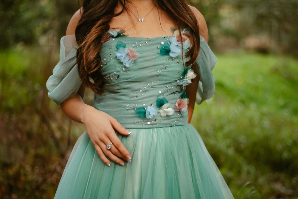 Beautiful mint green tulle gown with floral embellishments and off-shoulder sleeves photographed in a garden setting