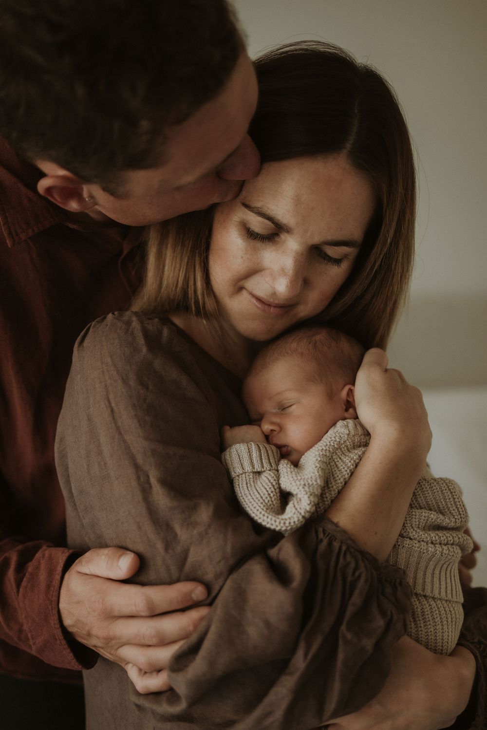 Intimate sequence of photos showing tender moments between parent and baby in soft, moody lighting.