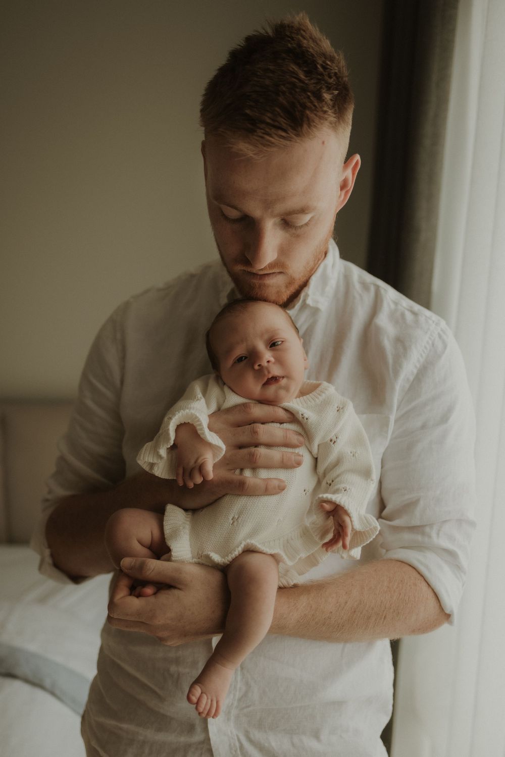 A tender moment between a parent in a white shirt cradling and kissing a small baby in white clothing.
