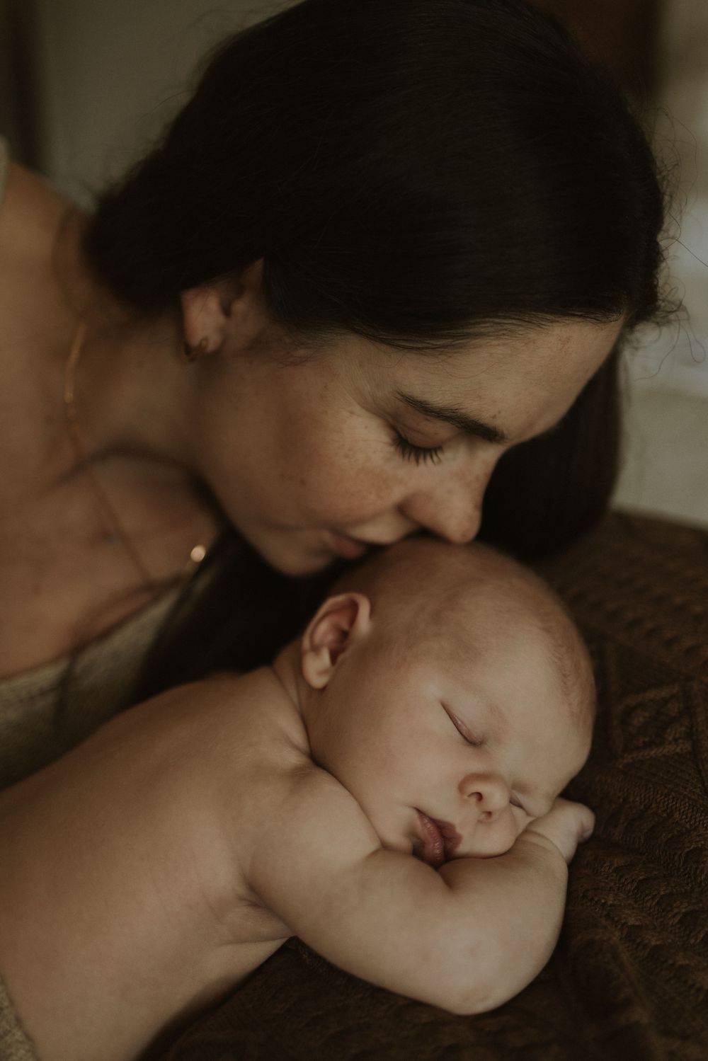 Tender moment between parent and sleeping newborn on textured surface.