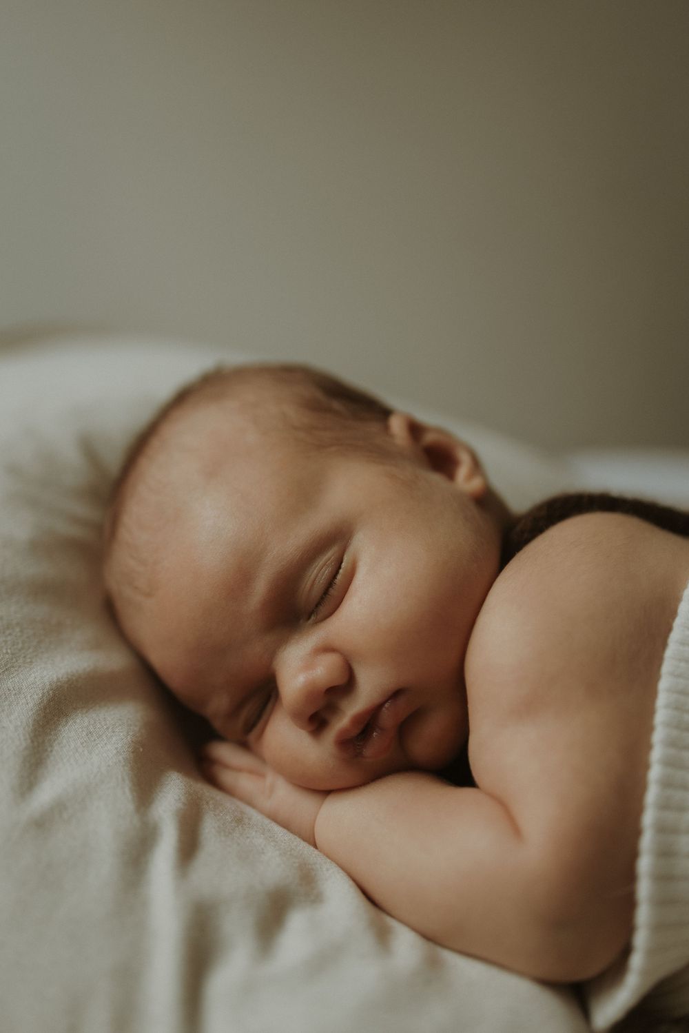 A peaceful sleeping baby rests on soft white bedding in a gentle natural light setting.
